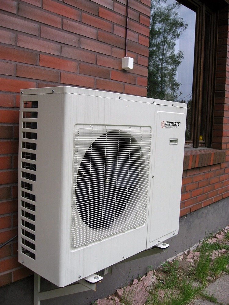 Unité extérieure d'une pompe à chaleur installée sur un mur de maison, illustrant l'électrification du chauffage